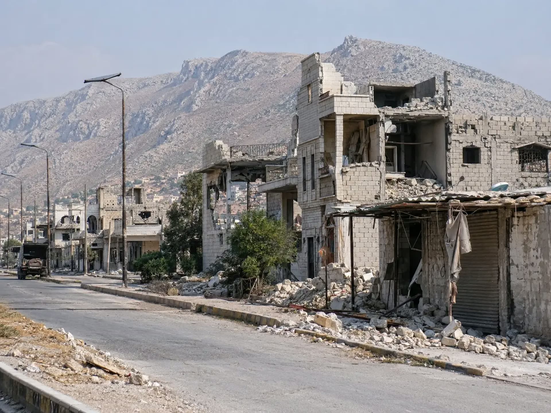 Damaged buildings along a road beneath the mountains.